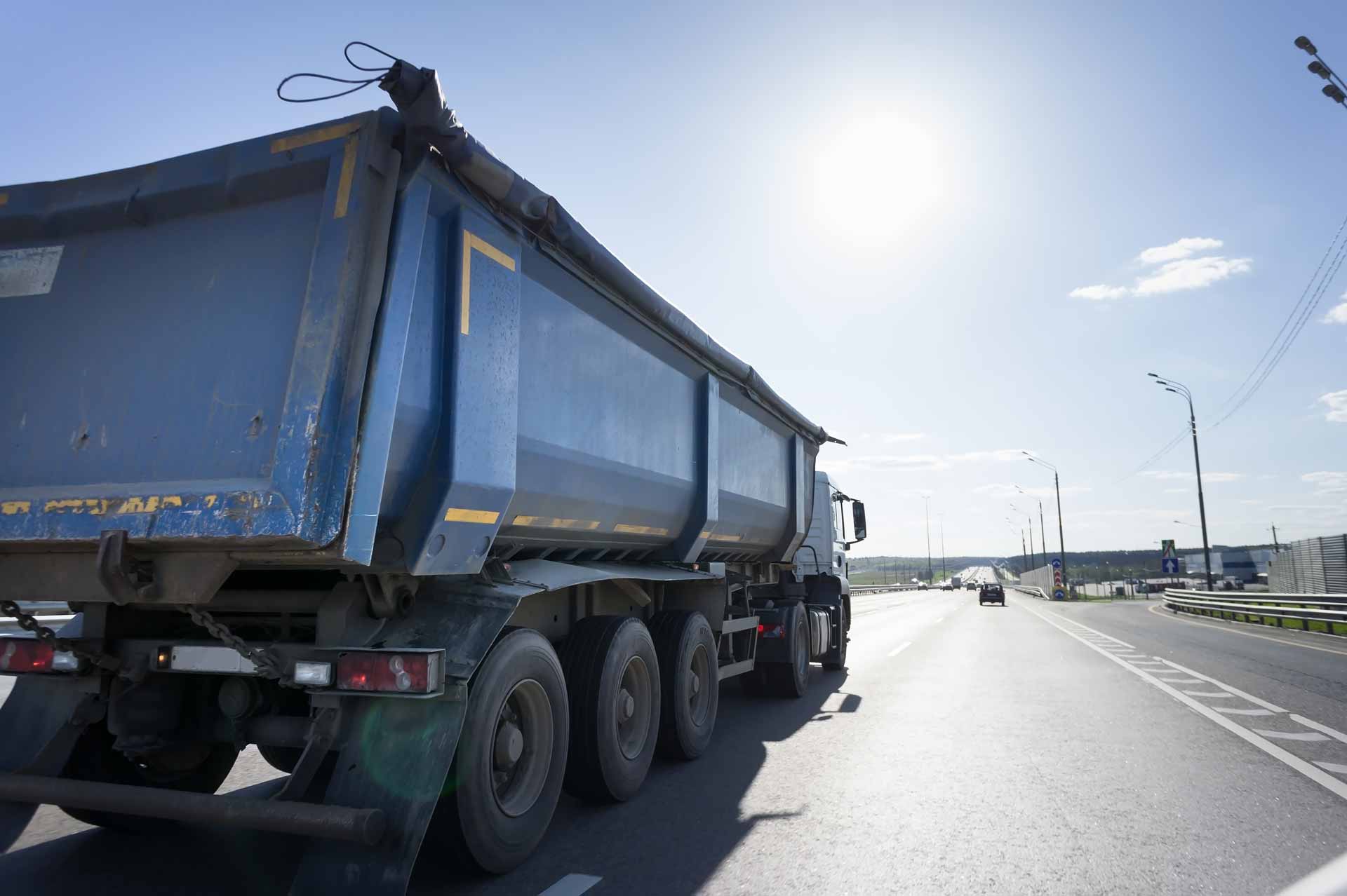 A blue dump truck driving down a road on a sunny day