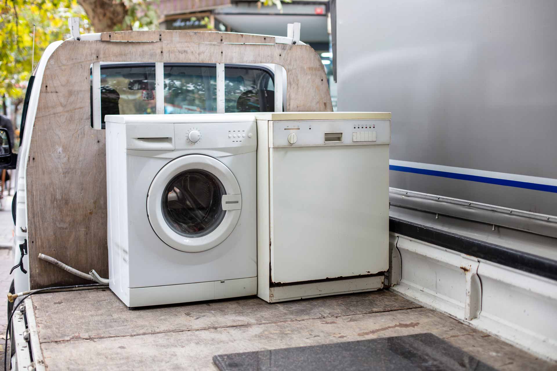 An old washing machine and dishwasher on the back of a dump truck