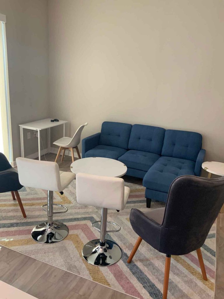 An assortment of living room furniture: a blue couch, several seats, and white end tables